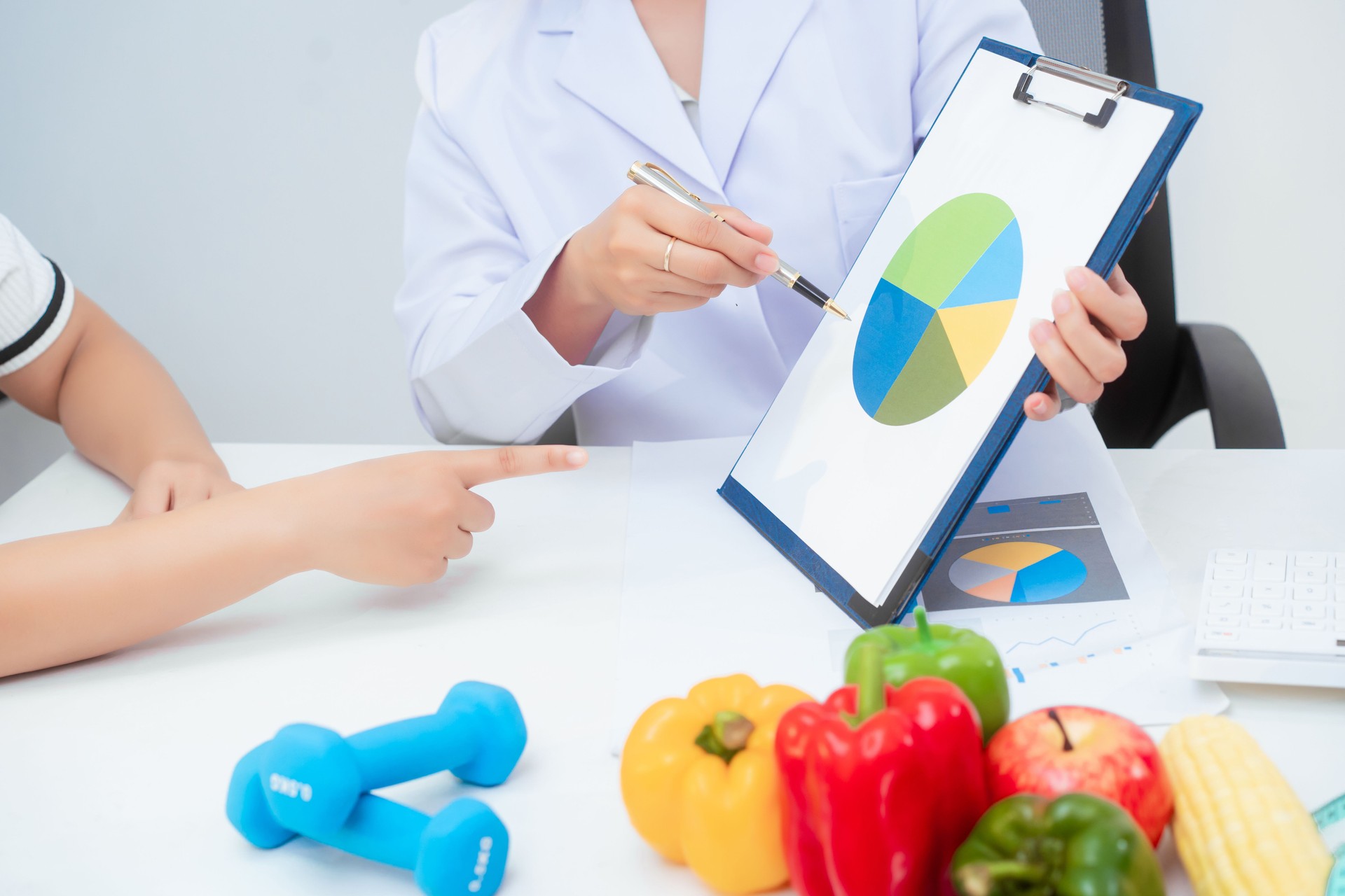 Professional Asian female nutritionist giving nutritional counseling to female patient sitting at clinic table discussing diet, health goals, meal plans and strategies for long-term wellness